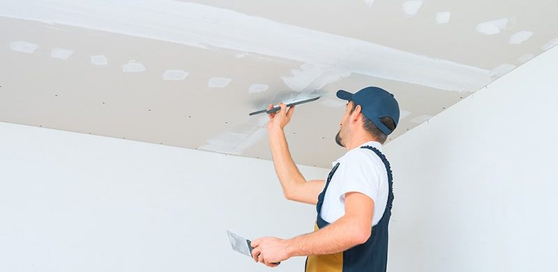 Worker finishing drywall on a ceiling.