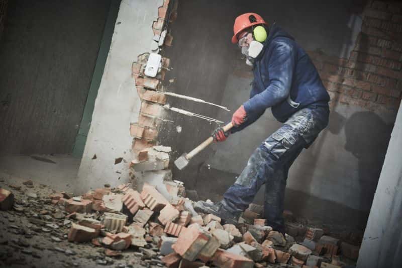 Trained worker demolishing a wall with a sledgehammer